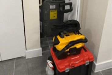 A yellow power tool sits atop a red toolbox and a black toolbox in a home hallway, indicating ongoing maintenance or repair work.